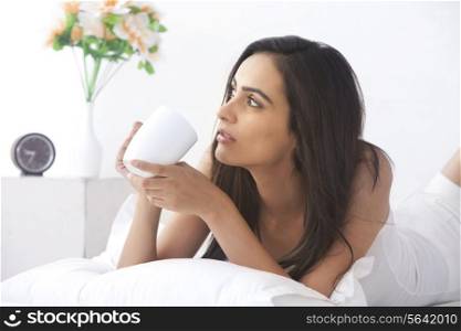 Thoughtful young woman having coffee in bed