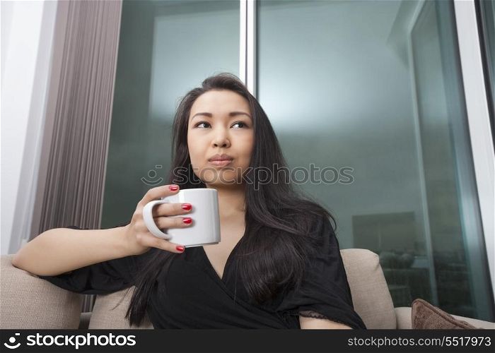 Thoughtful young woman having coffee in living room