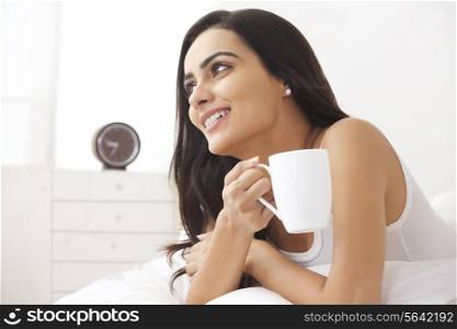 Thoughtful young woman holding coffee cup in bed