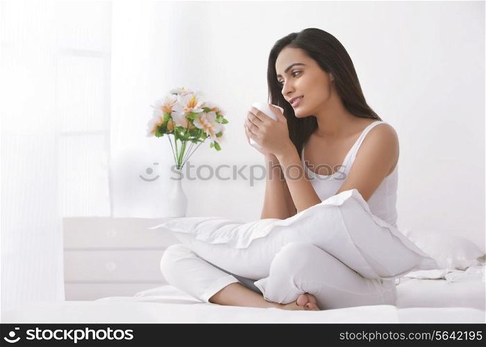 Thoughtful young woman holding coffee cup in bedroom