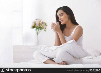 Thoughtful young woman holding coffee cup in bedroom
