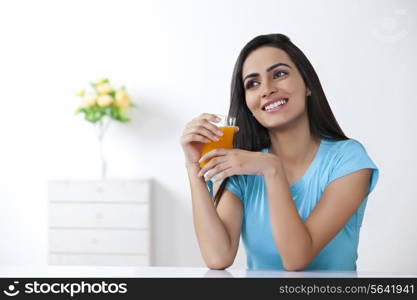 Thoughtful young woman holding glass of orange juice at home