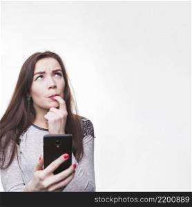 thoughtful young woman holding her mobile phone with her fingers mouth