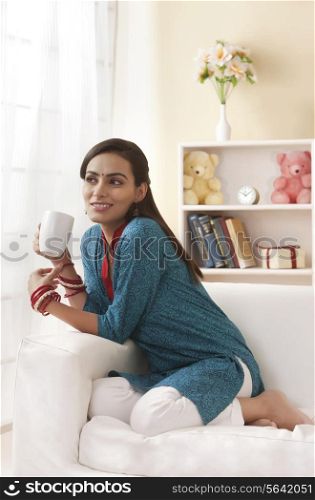 Thoughtful young woman in salwar kameez having coffee in living room