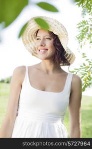 Thoughtful young woman in sundress and hat standing in park