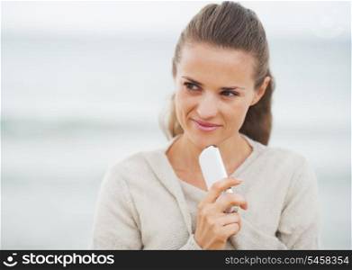 Thoughtful young woman in sweater on beach with cell phone
