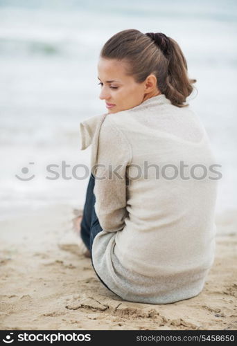 Thoughtful young woman in sweater sitting on lonely beach
