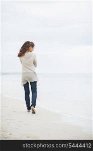 Thoughtful young woman in sweater walking on lonely beach . rear view