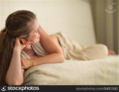 Thoughtful young woman laying on couch and looking on copy space