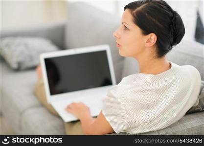 Thoughtful young woman laying on couch and using laptop