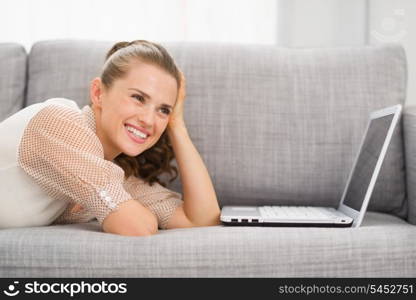 Thoughtful young woman laying on sofa with laptop