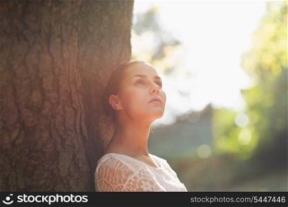 Thoughtful young woman lean against tree