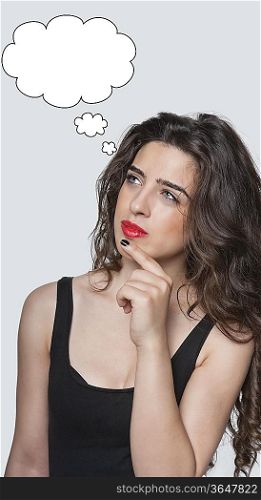 Thoughtful young woman looking at speech bubble with hand on chin over gray background