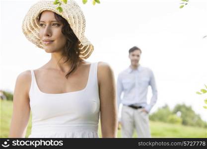 Thoughtful young woman looking away with man in background at park