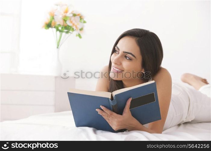 Thoughtful young woman reading book in bed