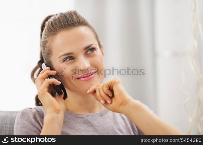 Thoughtful young woman sitting on couch and talking mobile phone