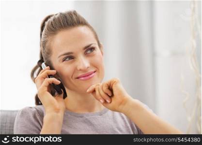 Thoughtful young woman sitting on couch and talking mobile phone