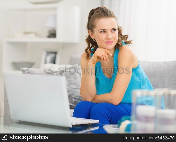 Thoughtful young woman sitting on couch and using laptop in living room