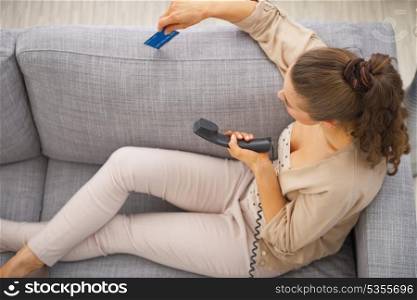 Thoughtful young woman sitting on couch with credit card and phone