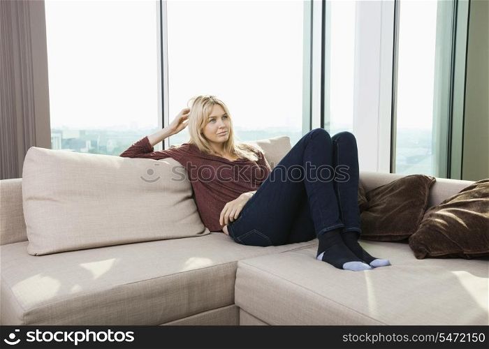 Thoughtful young woman sitting on sofa against window at home