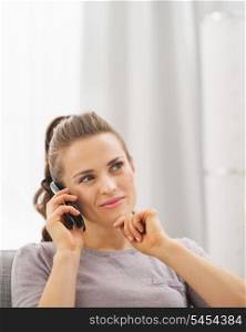 Thoughtful young woman sitting on sofa and talking cell phone