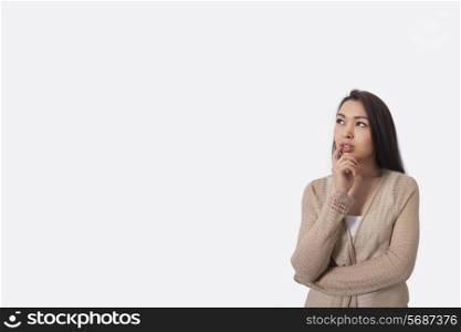 Thoughtful young woman standing against gray background