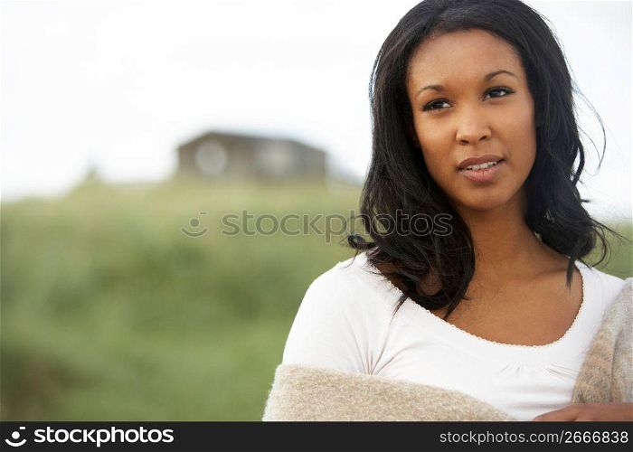Thoughtful Young Woman Standing On Beach Wrapped In Blanket