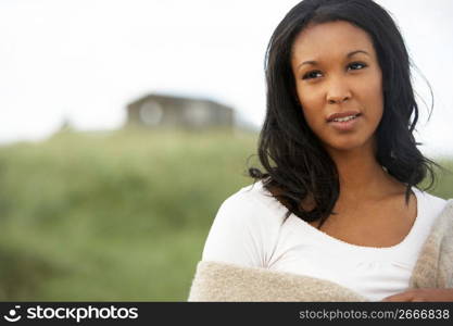 Thoughtful Young Woman Standing On Beach Wrapped In Blanket