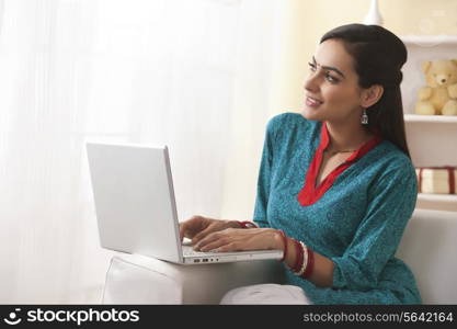 Thoughtful young woman using laptop on sofa