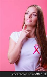 Thoughtful young woman wih pink cancer ribbon on chest. Healthcare, medicine and breast cancer awareness concept, light red background. Woman wih pink cancer ribbon on chest