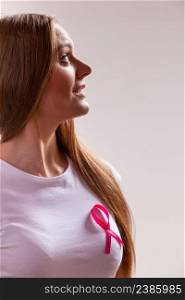 Thoughtful young woman wih pink cancer ribbon on chest looking away. Healthcare, medicine and breast cancer awareness concept, grey background. Woman wih pink cancer ribbon on chest