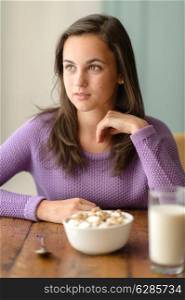 Thoughtful young woman with cereal breakfast wooden table looking aside