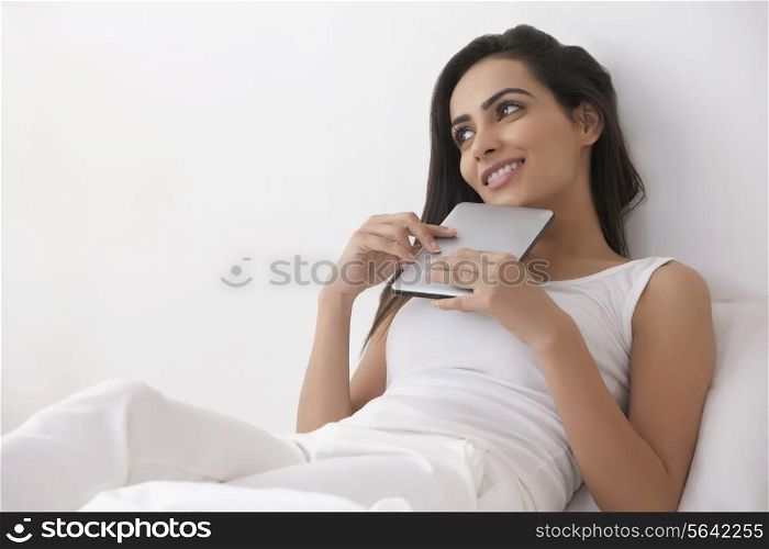 Thoughtful young woman with digital tablet in bedroom