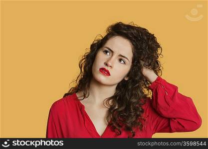 Thoughtful young woman with hand in hair over colored background