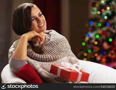 Thoughtful young woman with present box near christmas tree