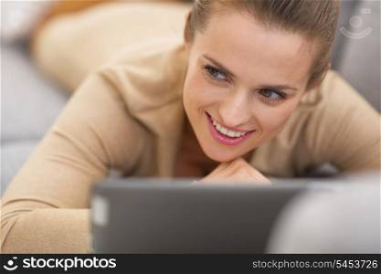 Thoughtful young woman with tablet pc laying on couch