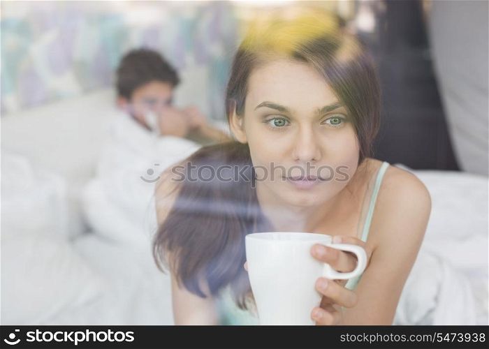 Thougtful woman having coffee at home with man lying in background