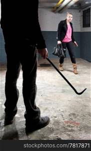 Threatening encounter in a basement, with a young woman trying to walk cautiously around an ominous figure holding a crowbar