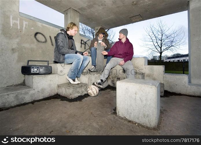 Three adolescent youths lighing cigarettes in a shelter in a suburbian area