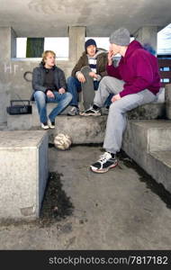 Three adolescent youths lighing cigarettes in a shelter in a suburbian area