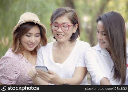 three asian woman looking on mobile phone screen with toothy smiling face