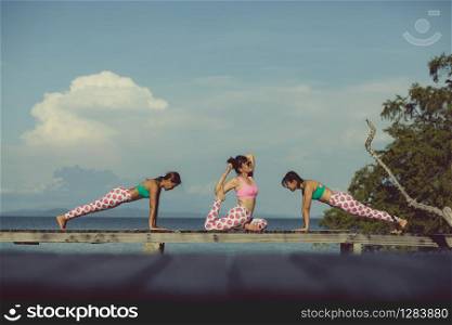three asian woman playing yoga flow on beach pier