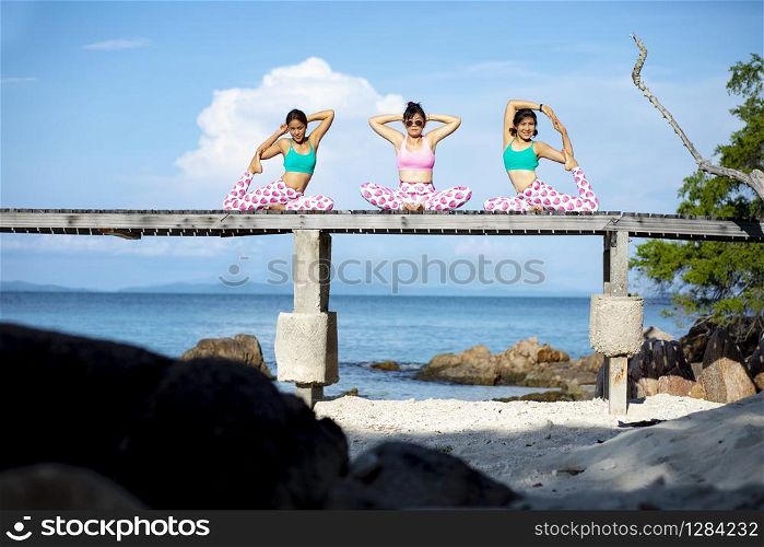 three asian woman playing yoga pose on beach pier