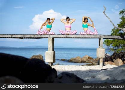 three asian woman playing yoga pose on beach pier