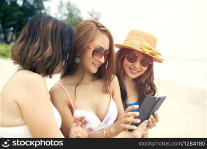 three asian woman relaxing on summer beach and taking selfie by smartphone