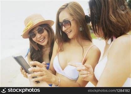 three asian woman relaxing on summer beach and taking selfie by smartphone