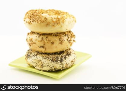 Three bagels stacked on green plate. Copy space on white background. Types are garlic, onion, and everything.