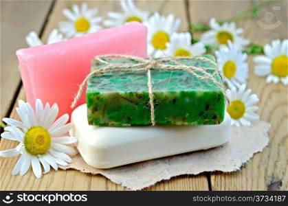 Three bars of soap pink, green and white on a piece of paper, daisy flowers on a background of wooden boards