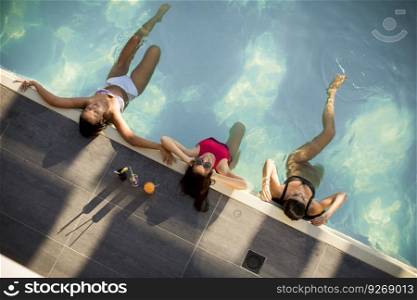 Three beautiful slim young women in bikini relaxing and drink cocktails on poolside of a swimming pool