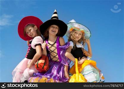 Three Beautiful Smiling Little Girls with Long Hair in the Colorful Witch Costumes Looking at Camera with Trick or Treat Bags.